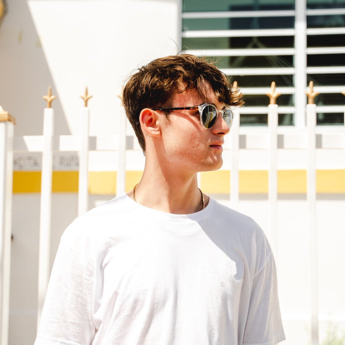 Person wearing sunglasses and a white t-shirt standing in front of a white picket fence.