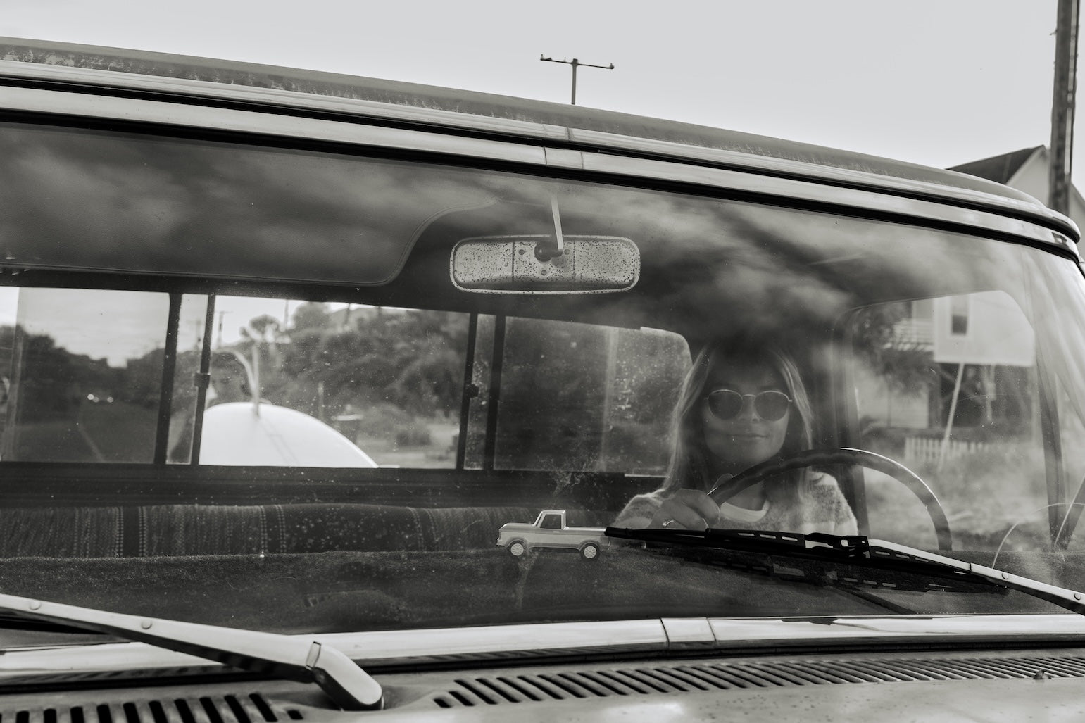 Person inside a car looking out the window with a reflection on the windshield.
