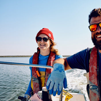 Two people on a boat in the water, wearing life vests and sunglasses.